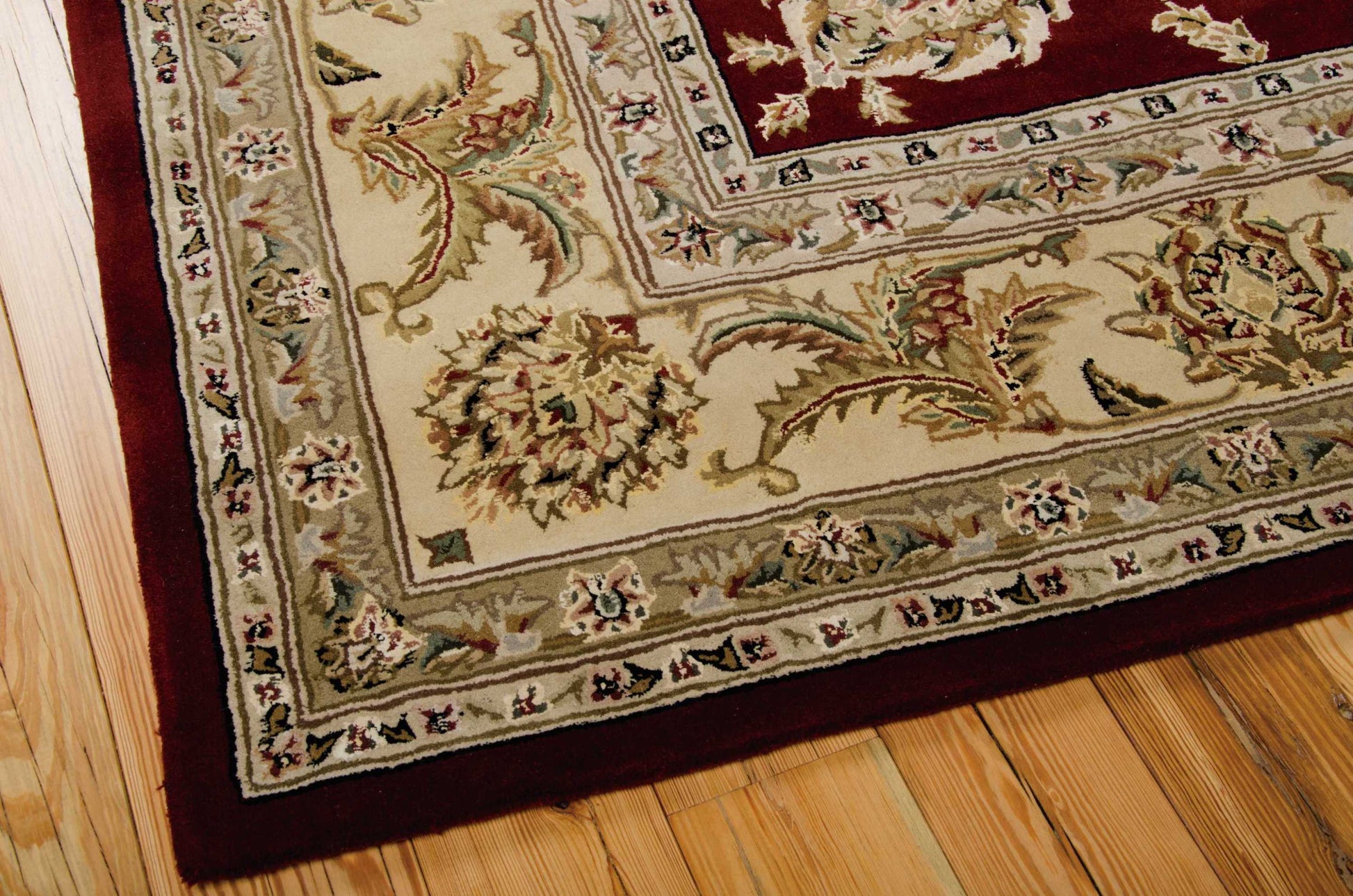 Cream oriental rug with intricate floral motifs and layered beige and burgundy borders on a wooden floor.