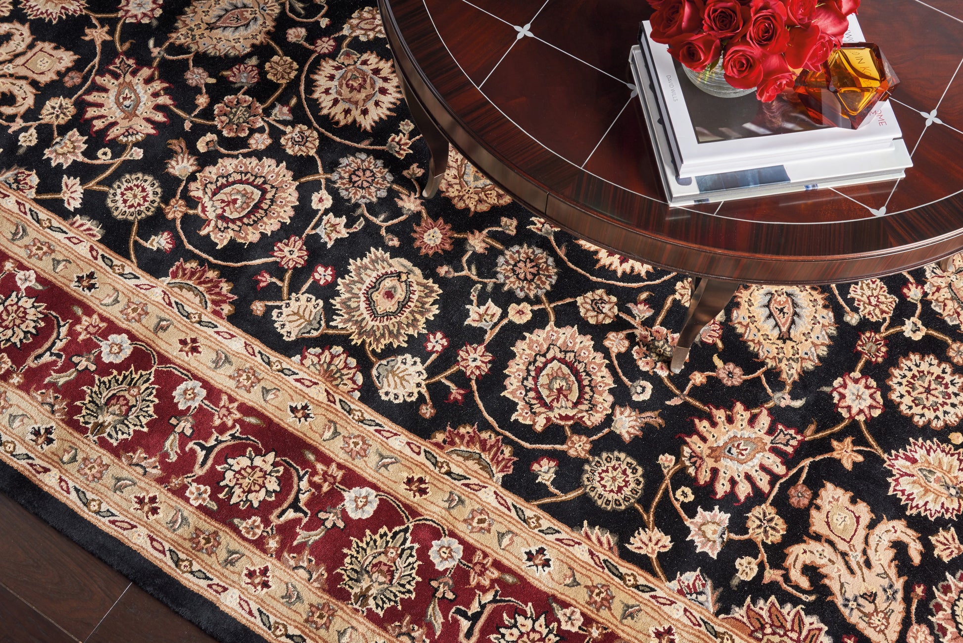 Persian-style black floral area rug with ivory and gold motifs, red border; wooden coffee table with books and red roses.