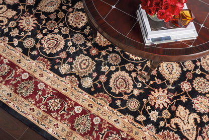 Black oriental rug with cream and gold floral motifs and a burgundy border; round dark wood coffee table with books and red roses on top.