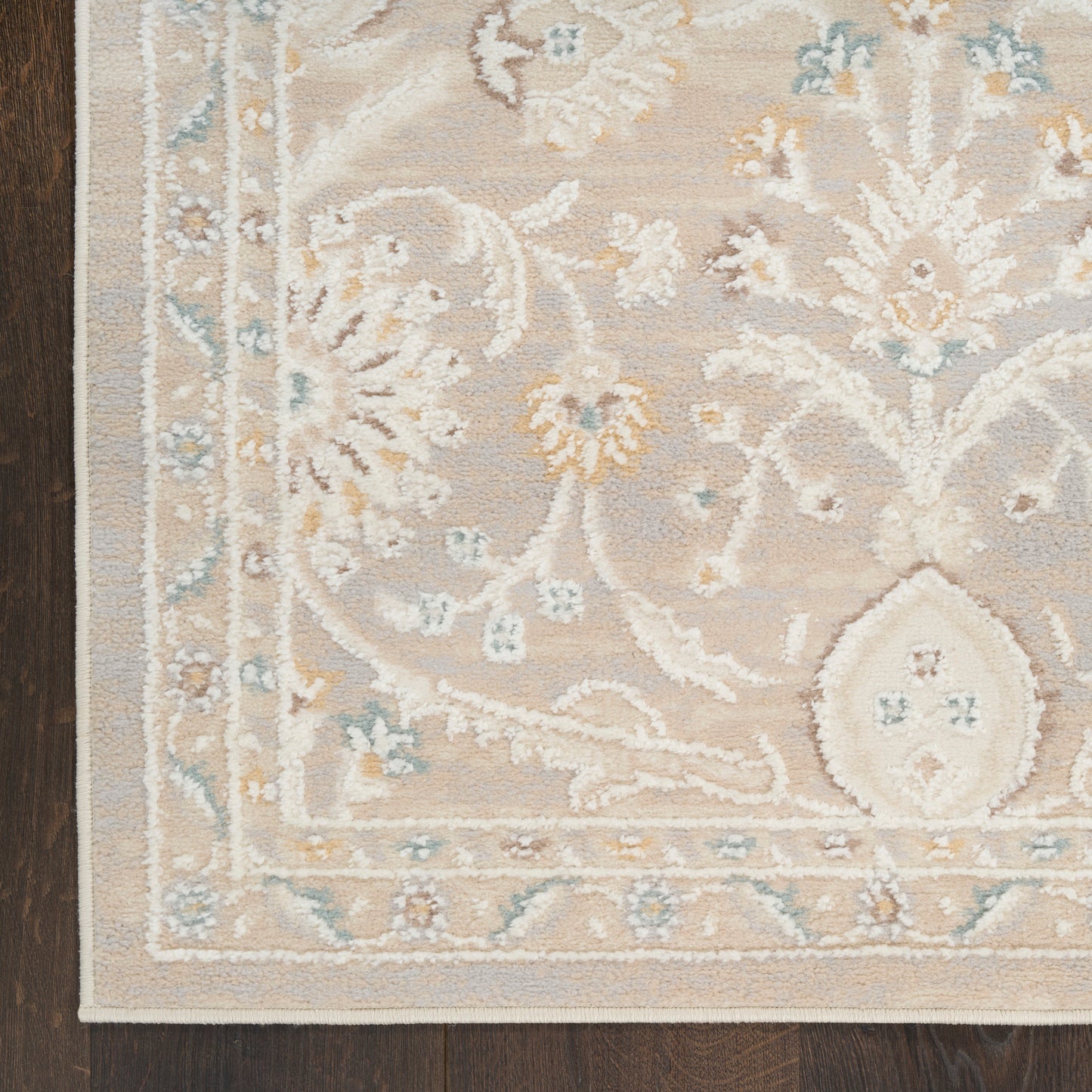 Beige oriental-style rug with pale blue and yellow floral motifs and a decorative border on a dark wood floor.
