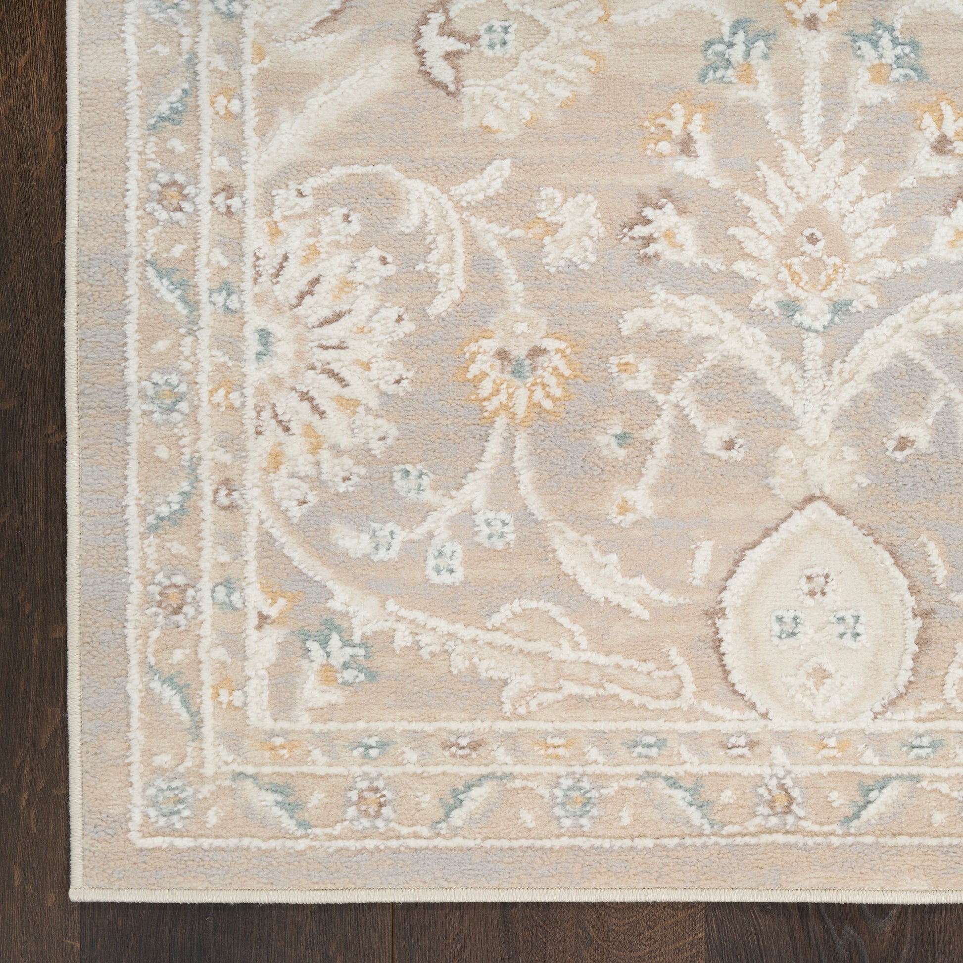 Beige oriental-style rug with pale blue and yellow floral motifs and a decorative border on a dark wood floor.