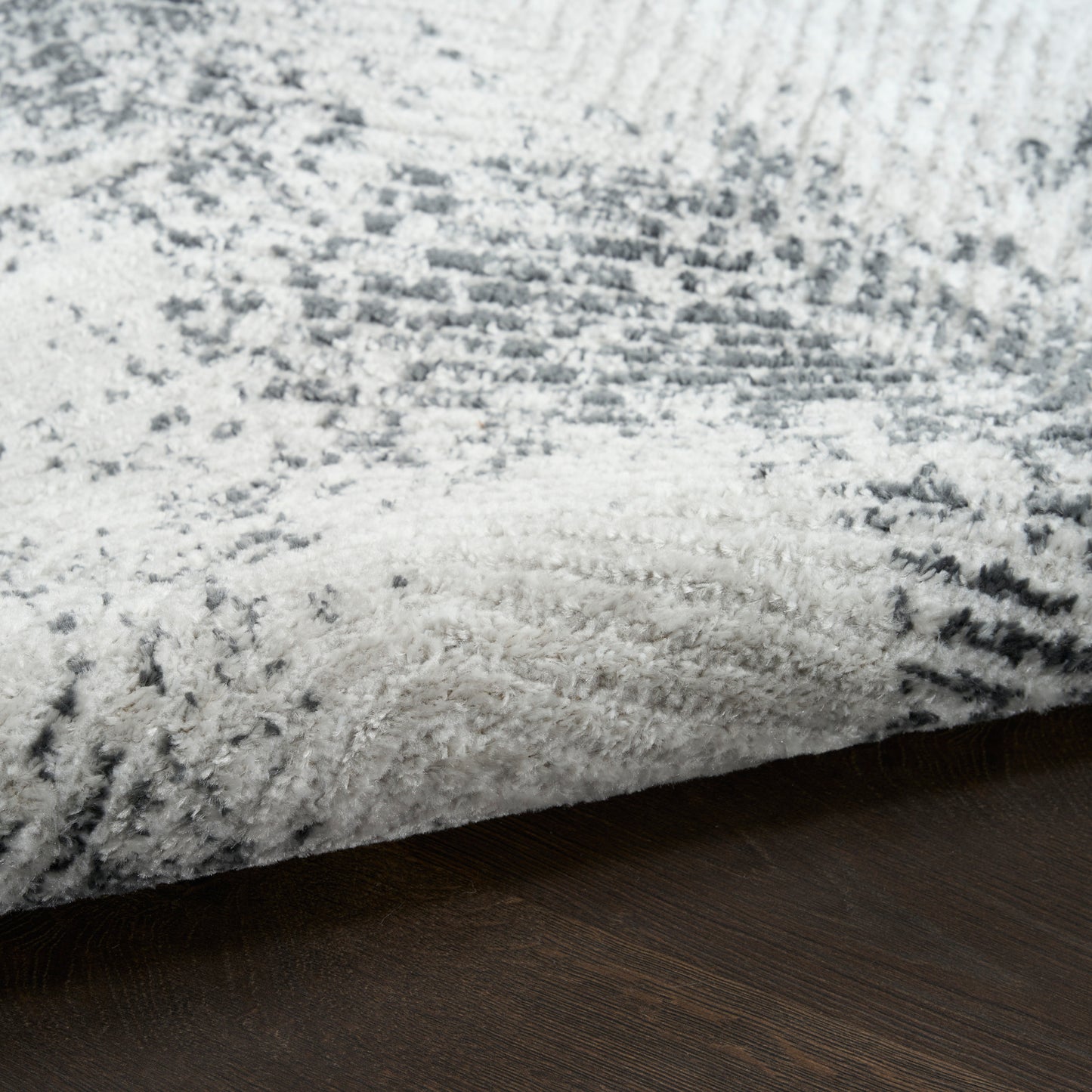 Plush gray and white shag rug with abstract pattern on dark wood floor; modern rectangular area rug.