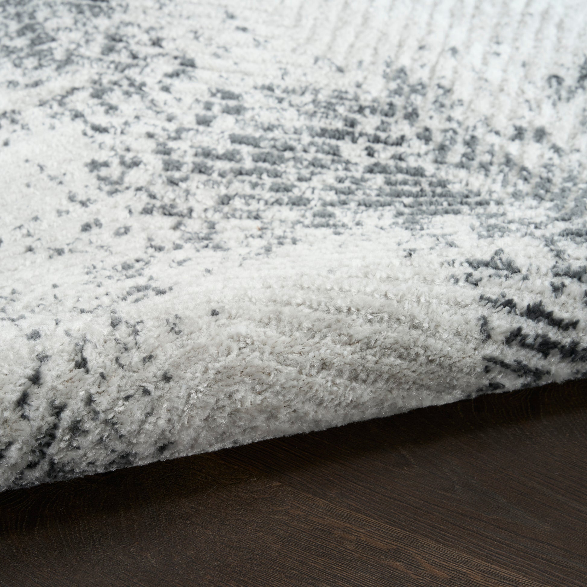 Plush gray and white shag rug with abstract pattern on dark wood floor; modern rectangular area rug.