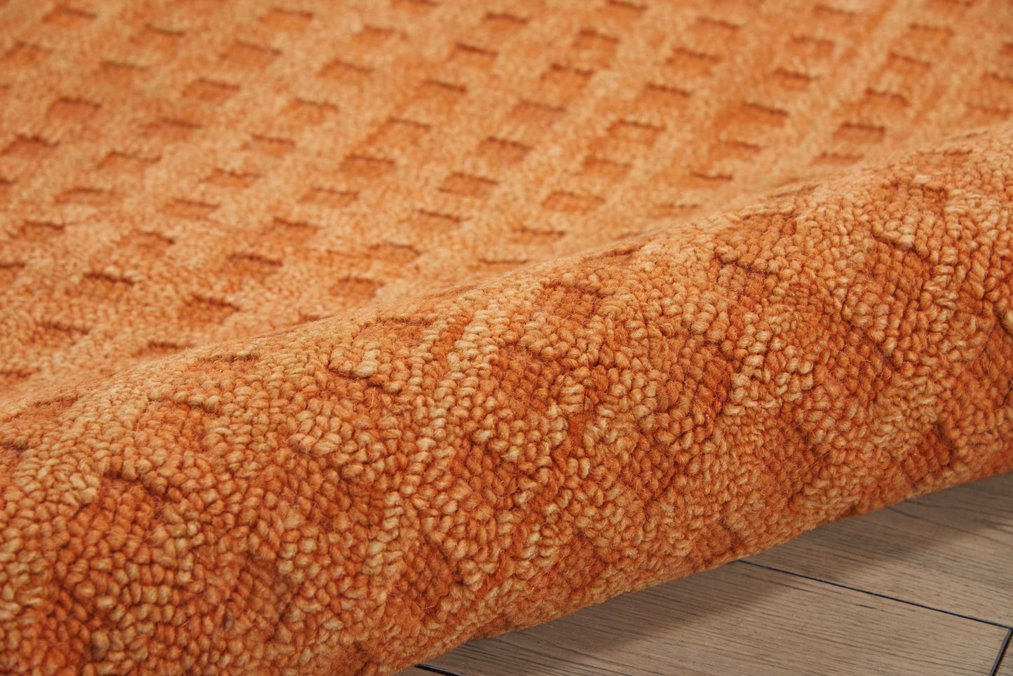 Orange boucle shag rug with chunky textured pile, rolled edge, on light wood floor.