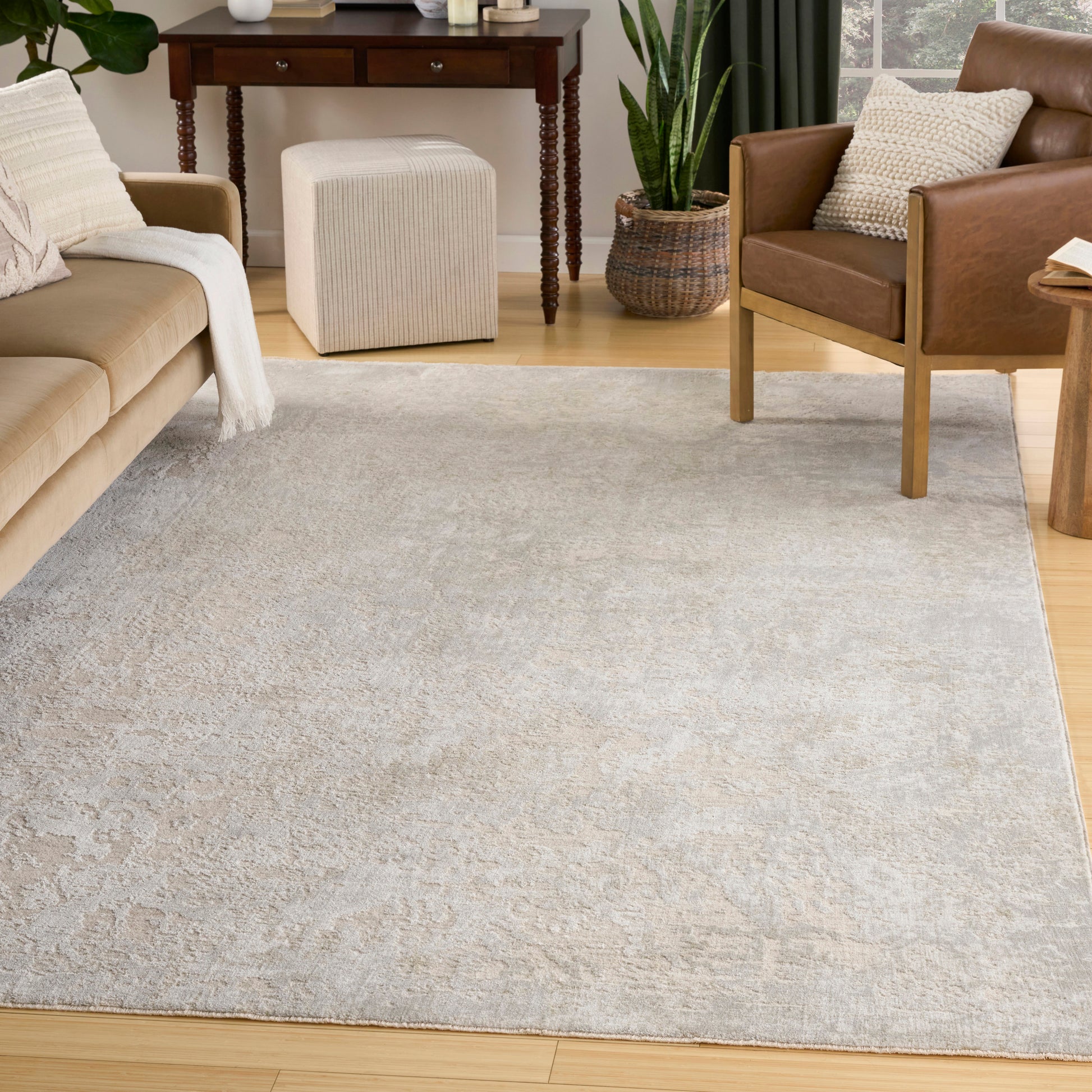 Large light gray patterned area rug on wood floor in a cozy living room with a tan sofa, brown leather chair, and greenery.