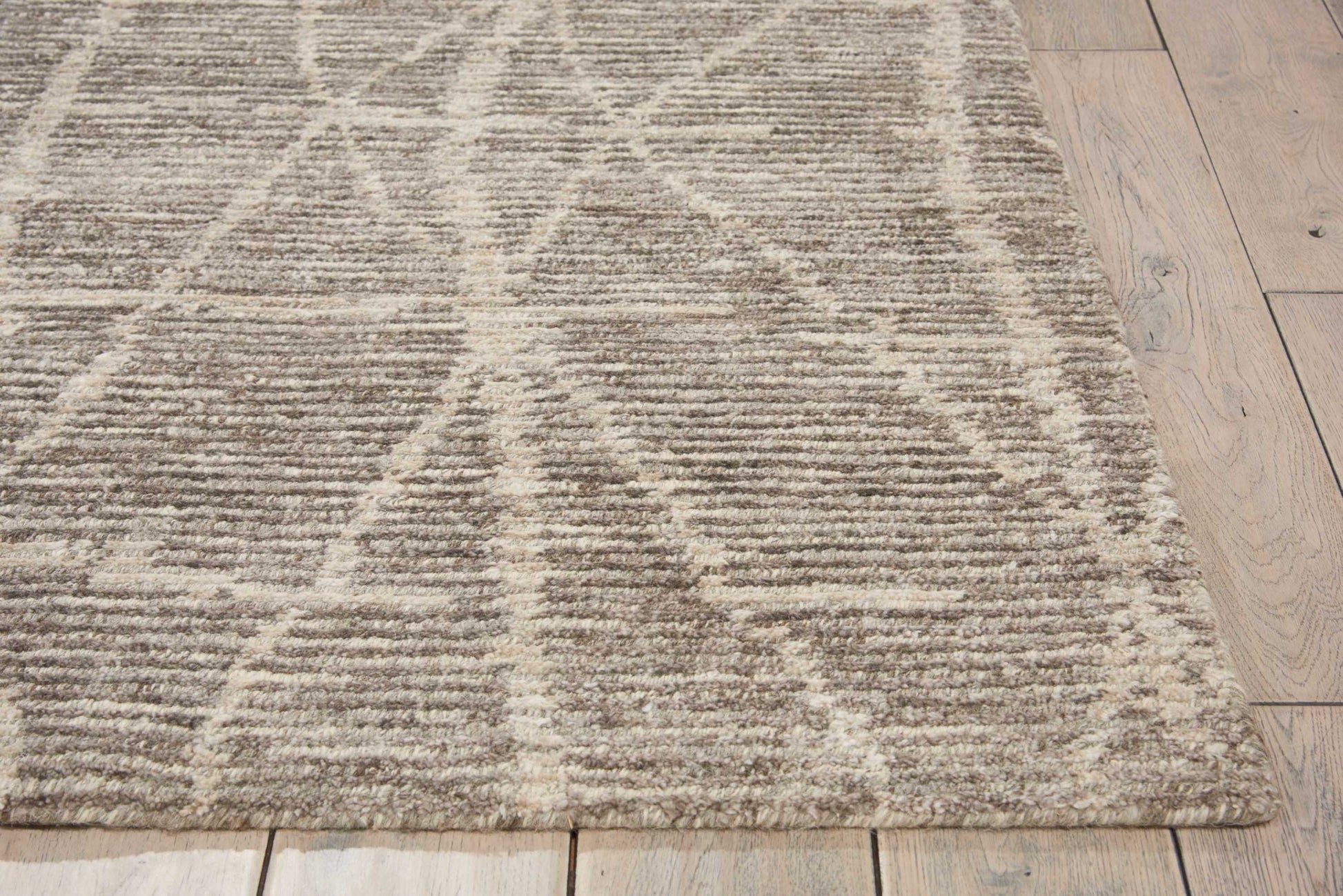 Beige-gray area rug with white geometric triangle pattern, plush pile on light wood floor; modern cozy style.