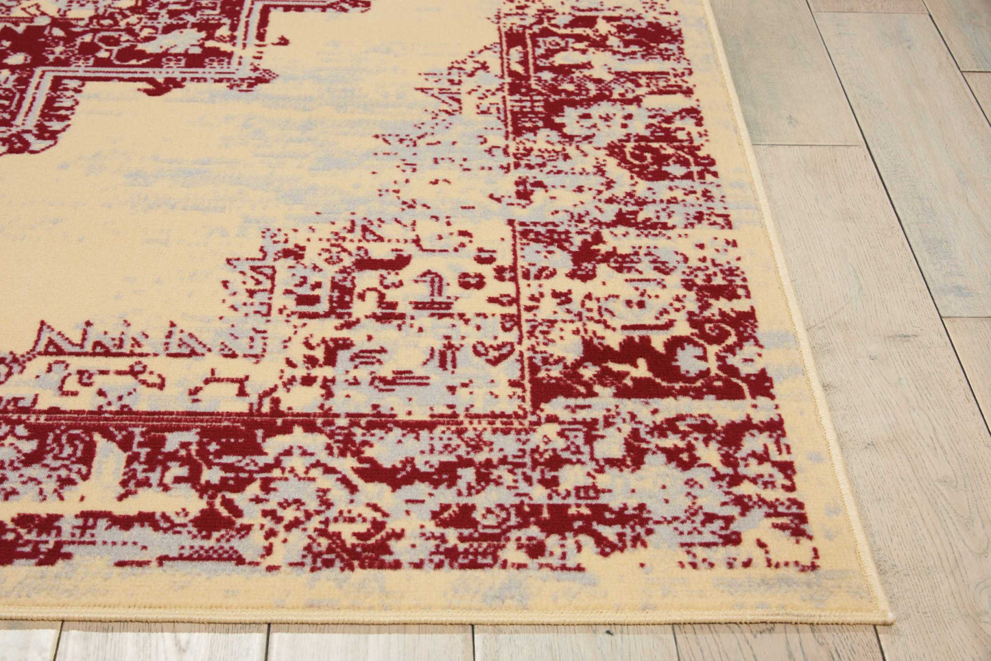 Beige distressed area rug with burgundy ornate border on light wood floor.