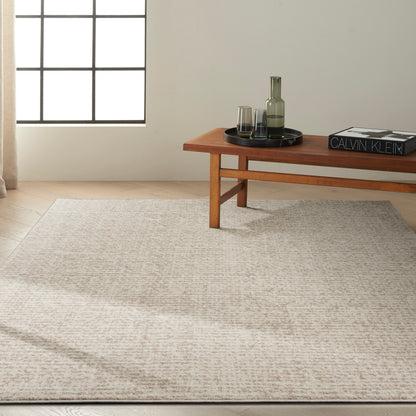 Beige textured rug with a low wooden coffee table on it, a black tray, glass carafe and glasses, and a decorative book.