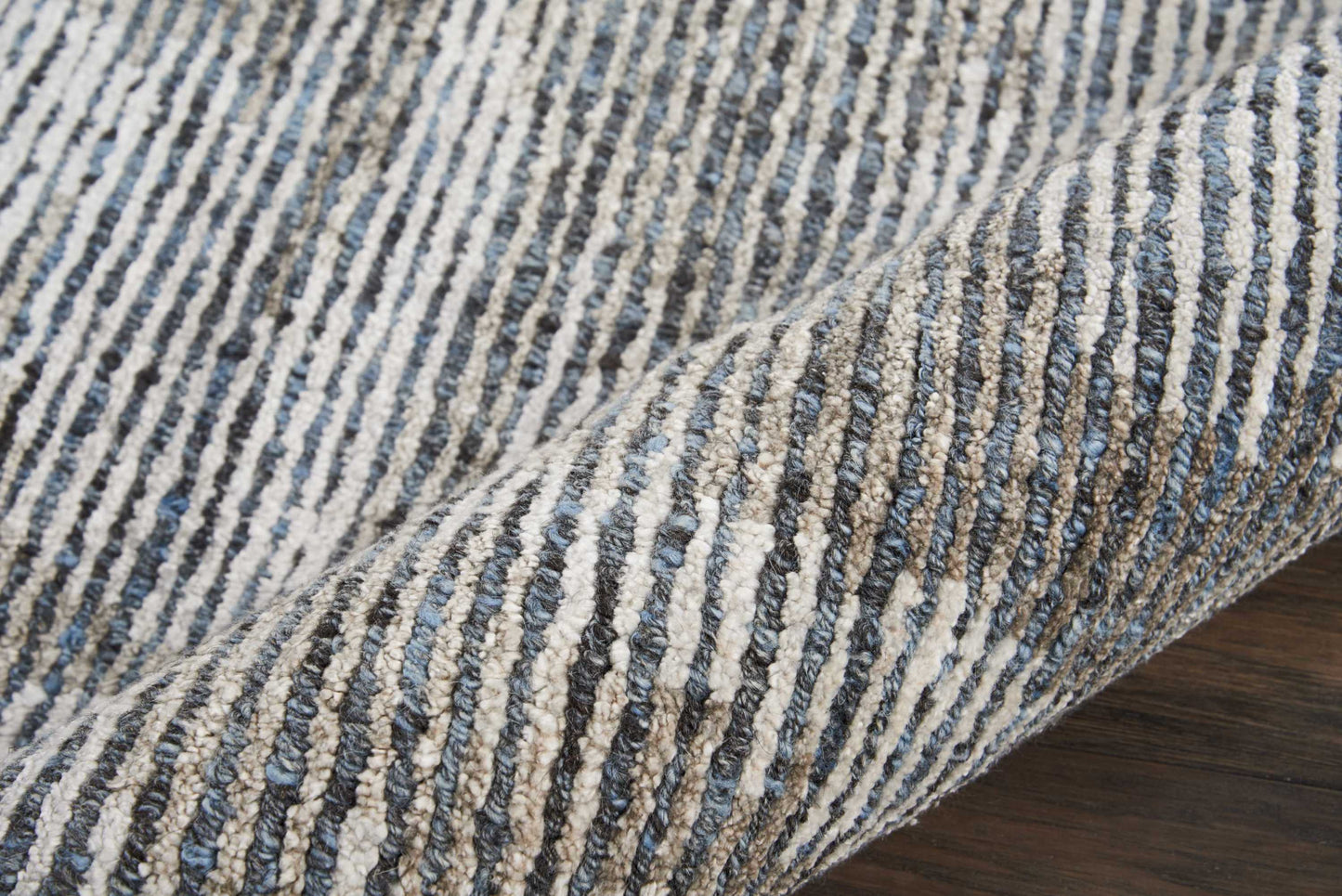 Blue and off-white striped woven rug with a textured loop pile, rolled on dark wood floor.