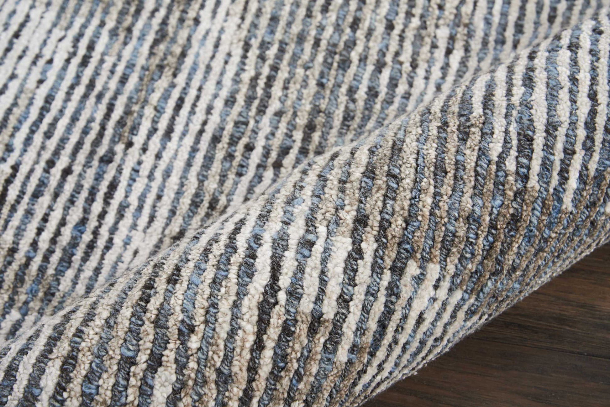 Blue and off-white striped woven rug with a textured loop pile, rolled on dark wood floor.