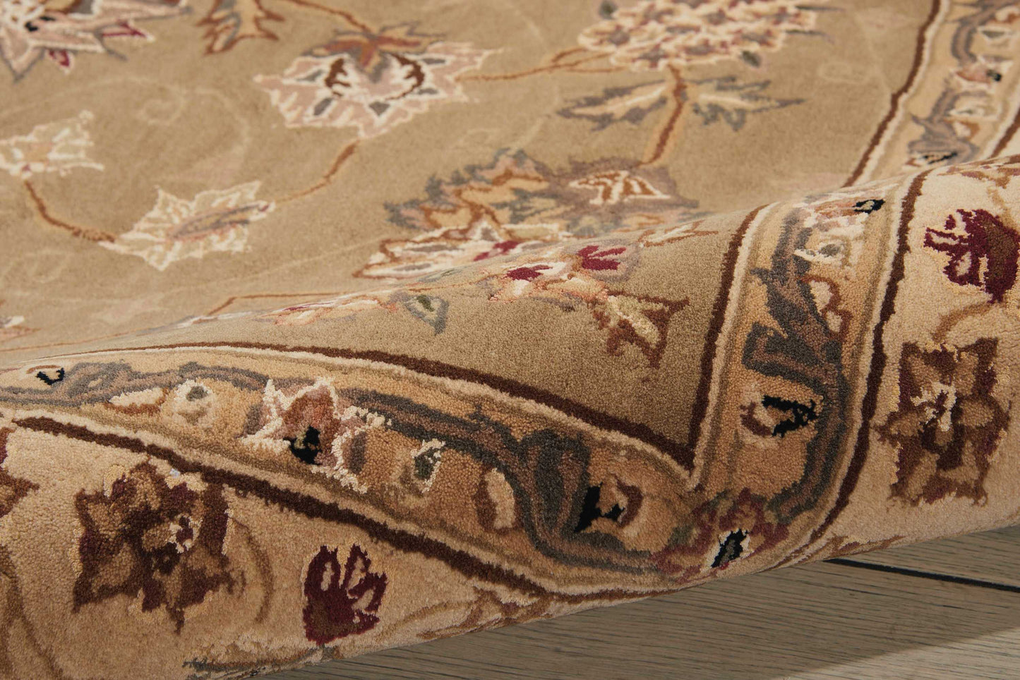 Beige oriental floral rug with cream, brown and burgundy accents, folded edge on wooden floor.