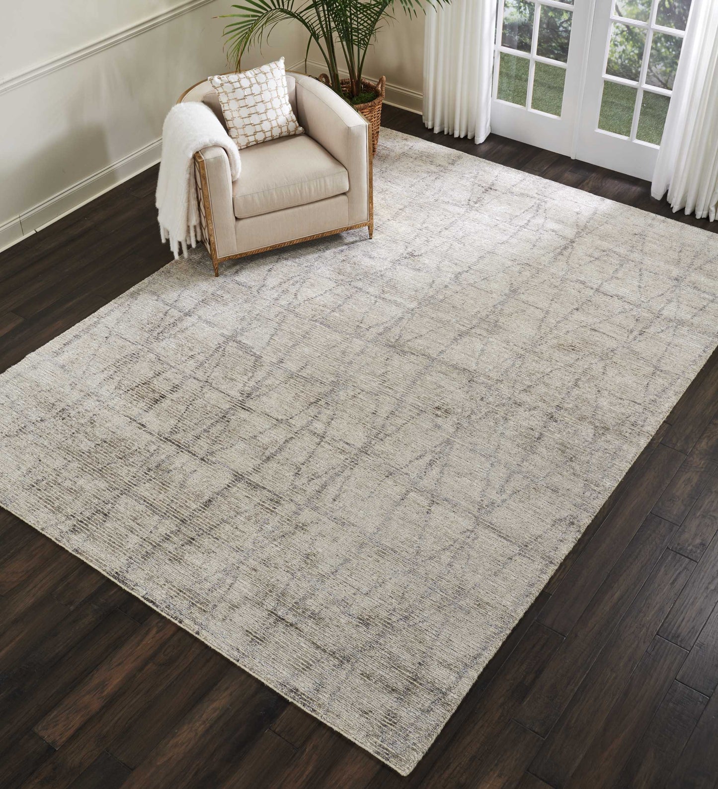 Beige area rug with subtle distressed gray pattern under a cream armchair with a wooden frame in a bright living room.