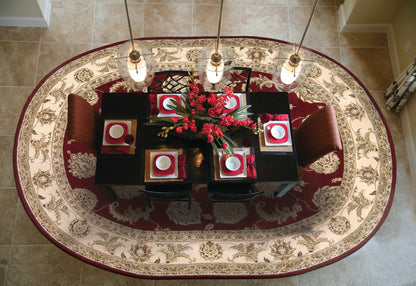 Top-down view of a dark dining table on an ornate round rug, red napkins, white plates, red centerpiece, and pendant lights.