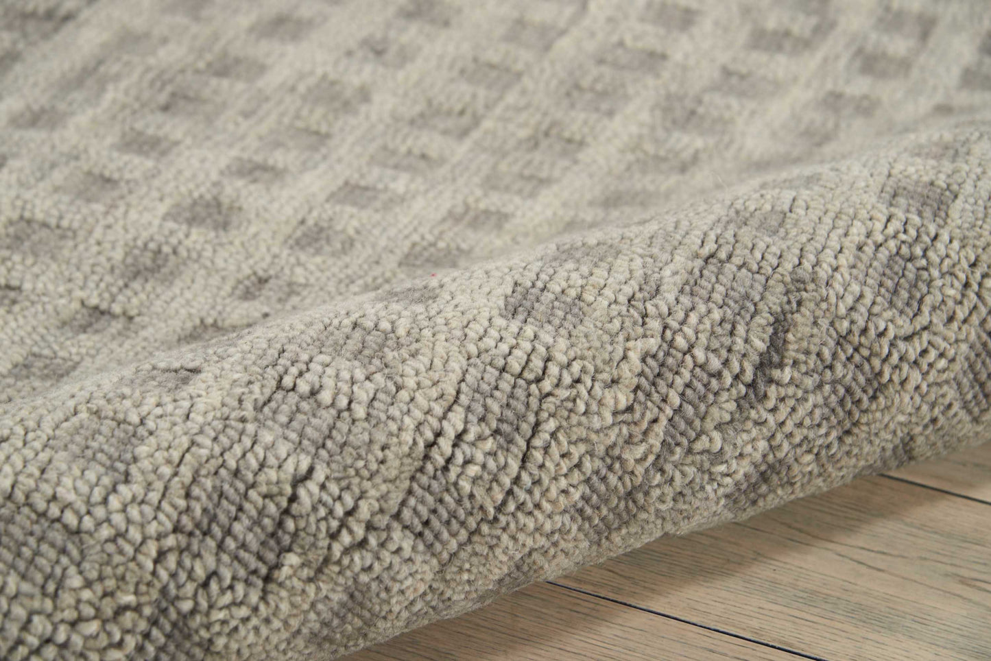 Soft gray textured loop-pile rug with subtle beige tones, rolled edge on light wooden floor.