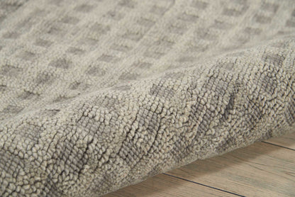 Soft gray textured loop-pile rug with subtle beige tones, rolled edge on light wooden floor.