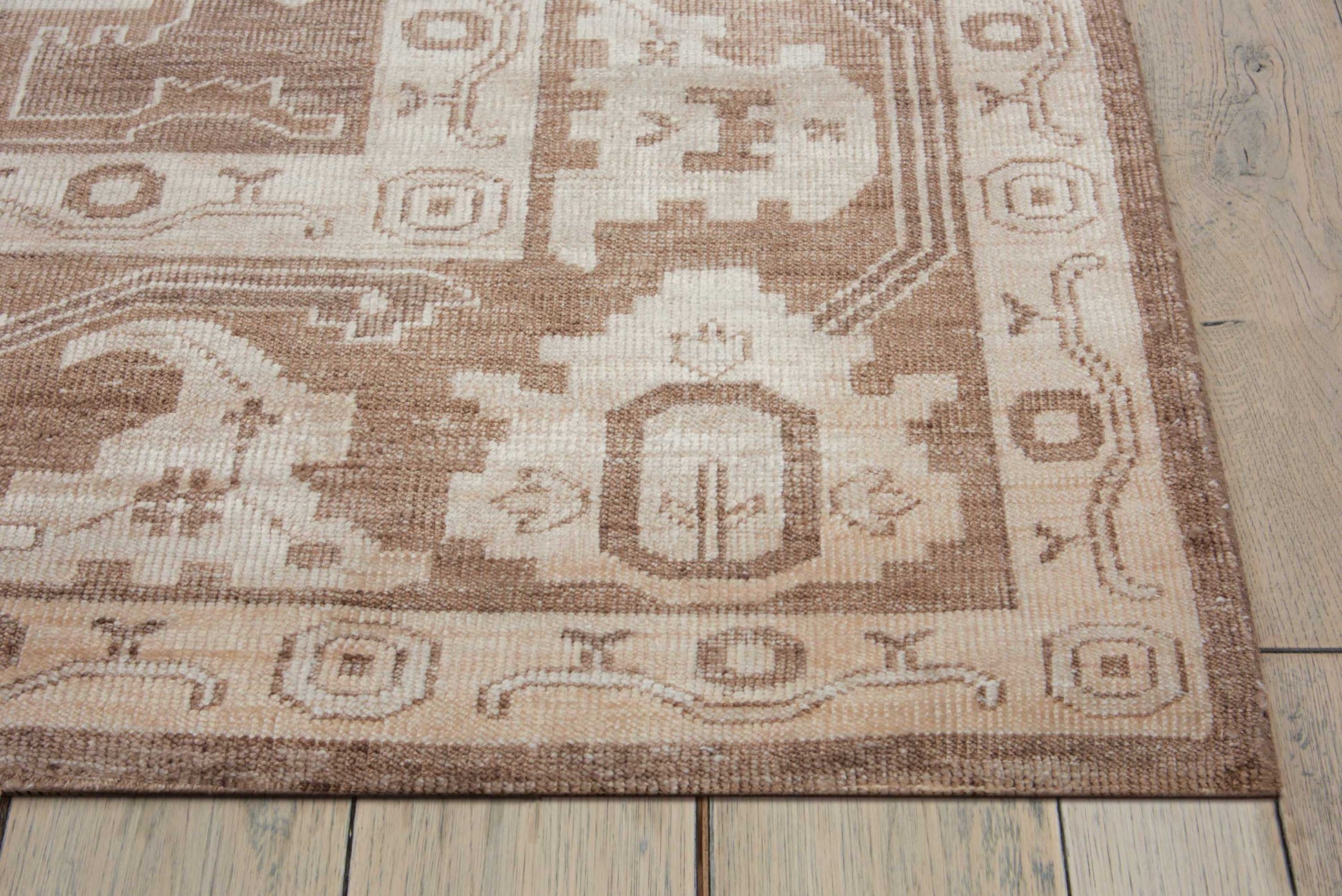 Rectangular beige-brown oriental rug with cream geometric medallions on a light wood floor.