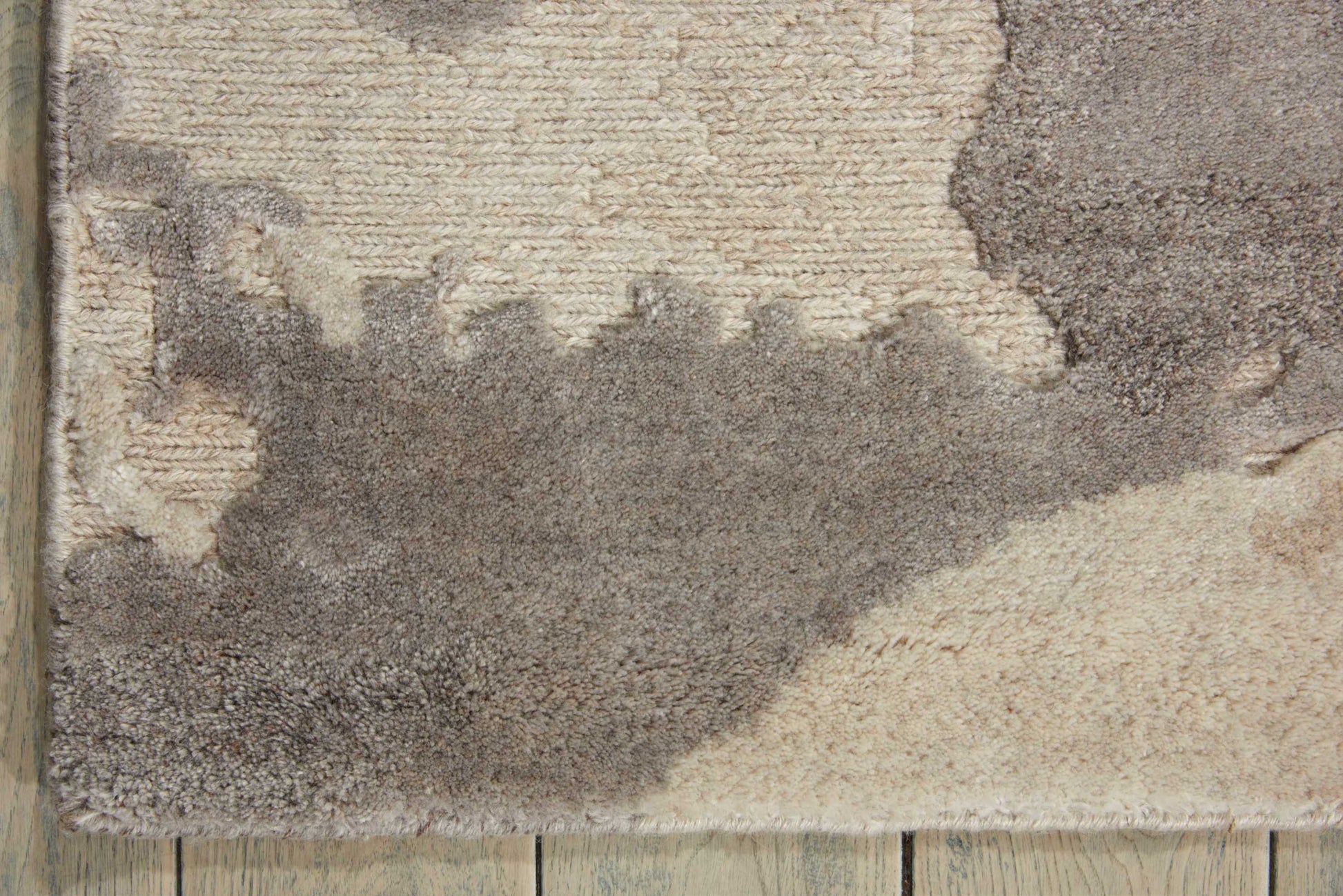 Textured shag rug with beige, taupe and gray abstract shapes on a light wood floor.