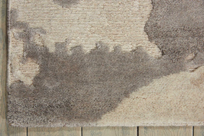 Textured shag rug with beige, taupe and gray abstract shapes on a light wood floor.