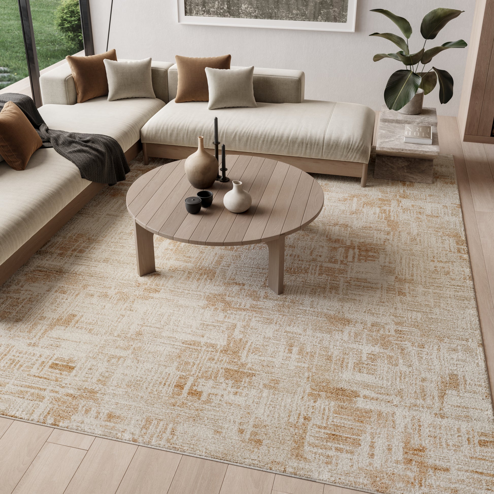 Round slatted wooden coffee table on a beige patterned rug with an L-shaped sofa, tan/gray cushions & a potted plant