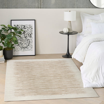 Neutral bedroom corner with white bedding, beige rug, black round side table, white lamp, framed art, and potted plant.