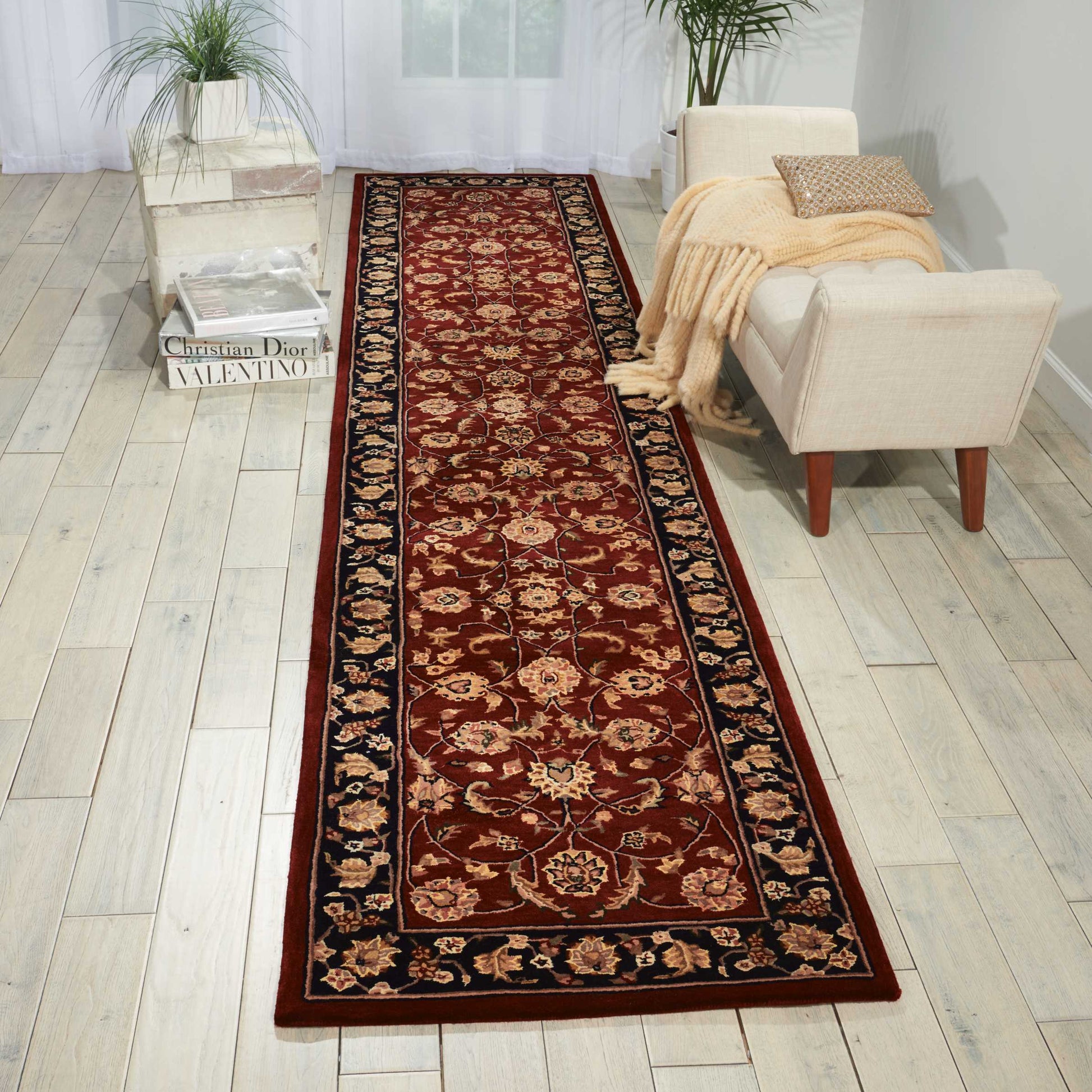 Long burgundy oriental runner rug with gold floral motifs and dark border, laid in a light living room with beige sofa.