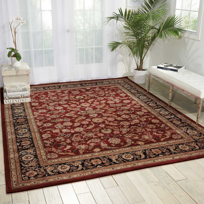 Large red Persian-style area rug with gold floral motifs and dark blue border in a bright, sunlit living room.