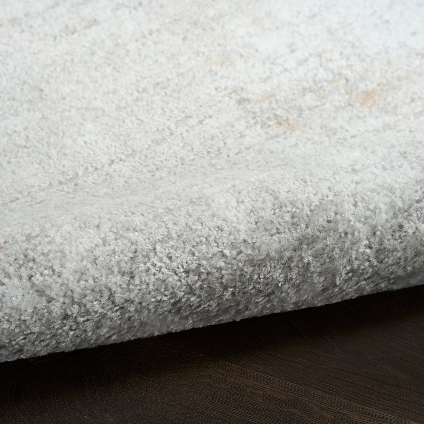 Light gray plush shag rug edge with fluffy texture on dark wood floor.