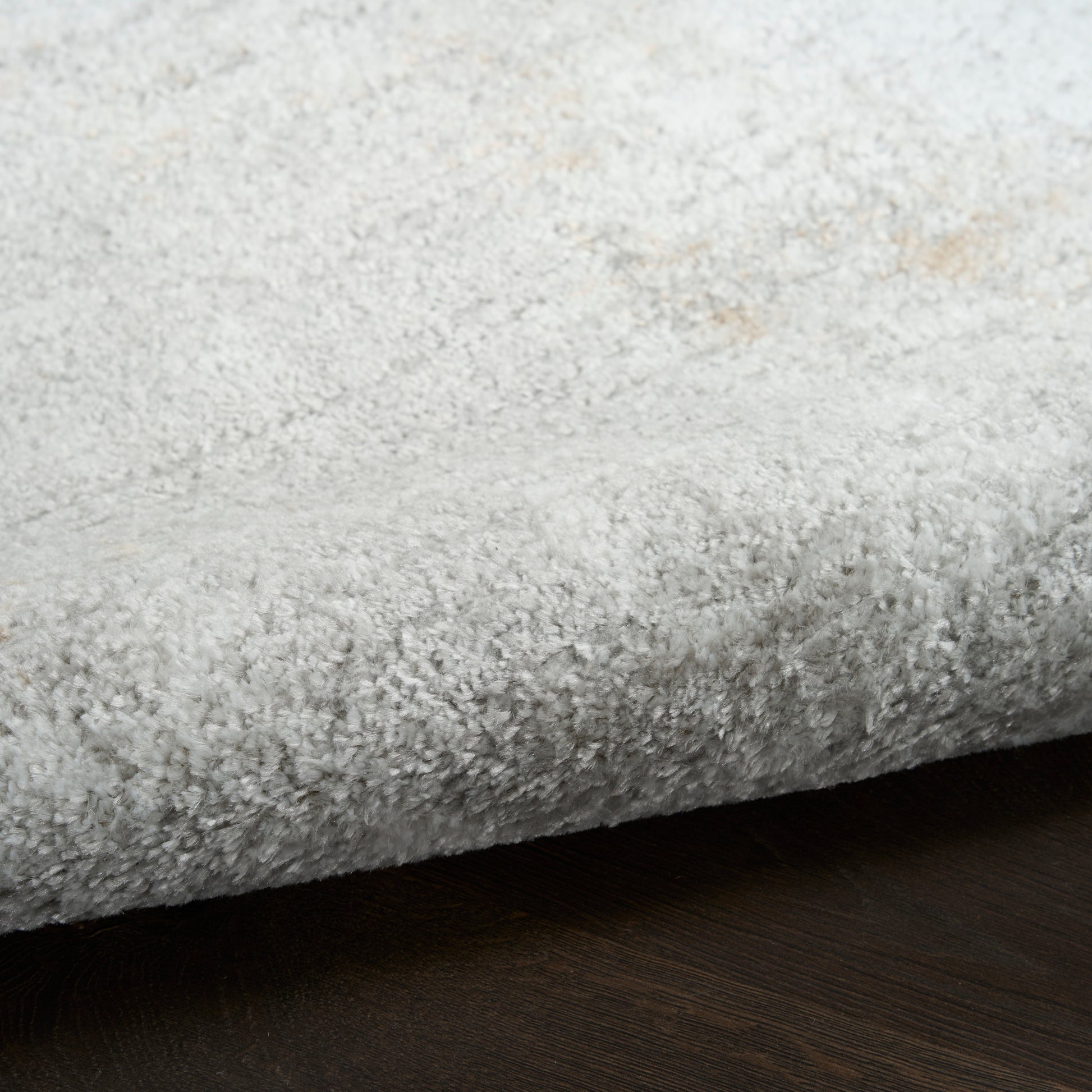 Light gray plush shag rug edge with fluffy texture on dark wood floor.