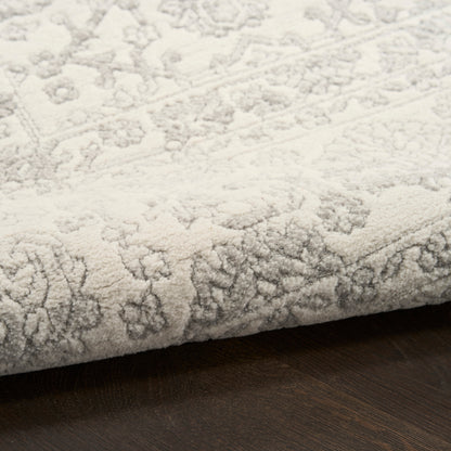 Cream patterned rug with subtle floral motif and soft pile, folded edge on dark wood floor.