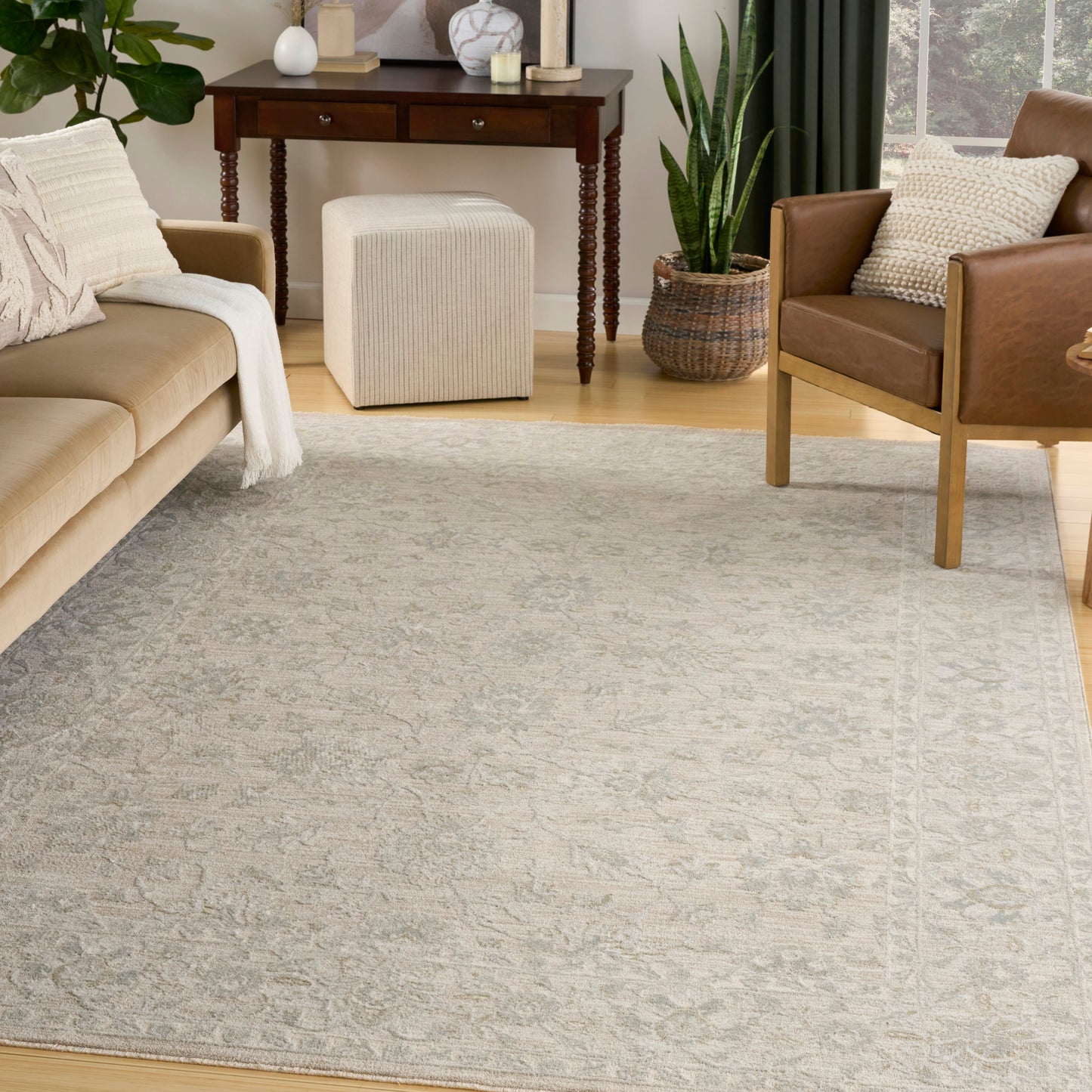 Light gray patterned area rug anchors a cozy living room with beige sofa, tan leather chair, white pouf ottoman, and plants.