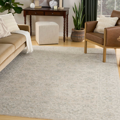 Light gray patterned area rug anchors a cozy living room with beige sofa, tan leather chair, white pouf ottoman, and plants.
