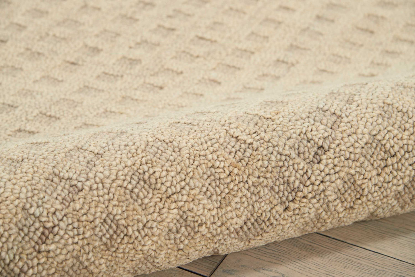 Beige boucle shag rug with dense loop pile, rolled edge, laid on light wooden floor.