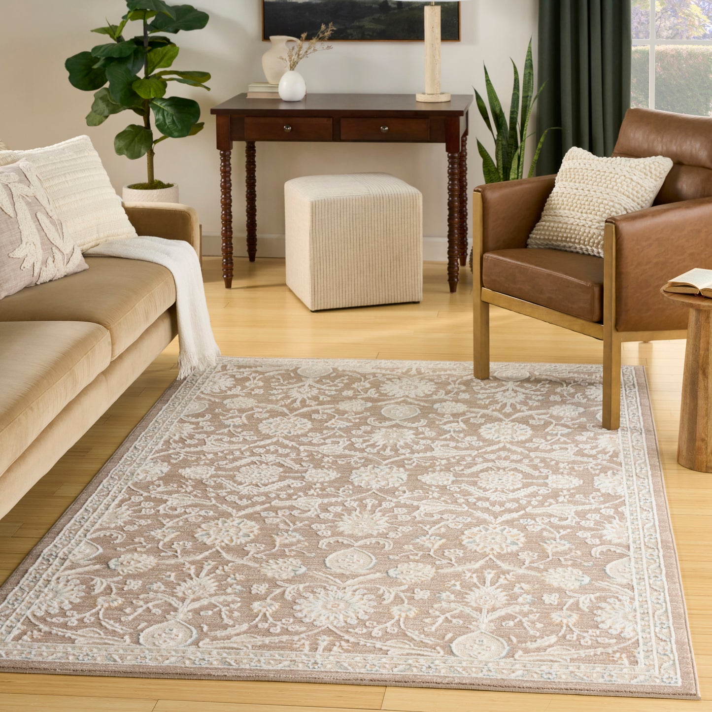 Cozy living room: beige fabric sofa, brown leather chair, cream floral area rug with border, light wood floor, dark wood console table.