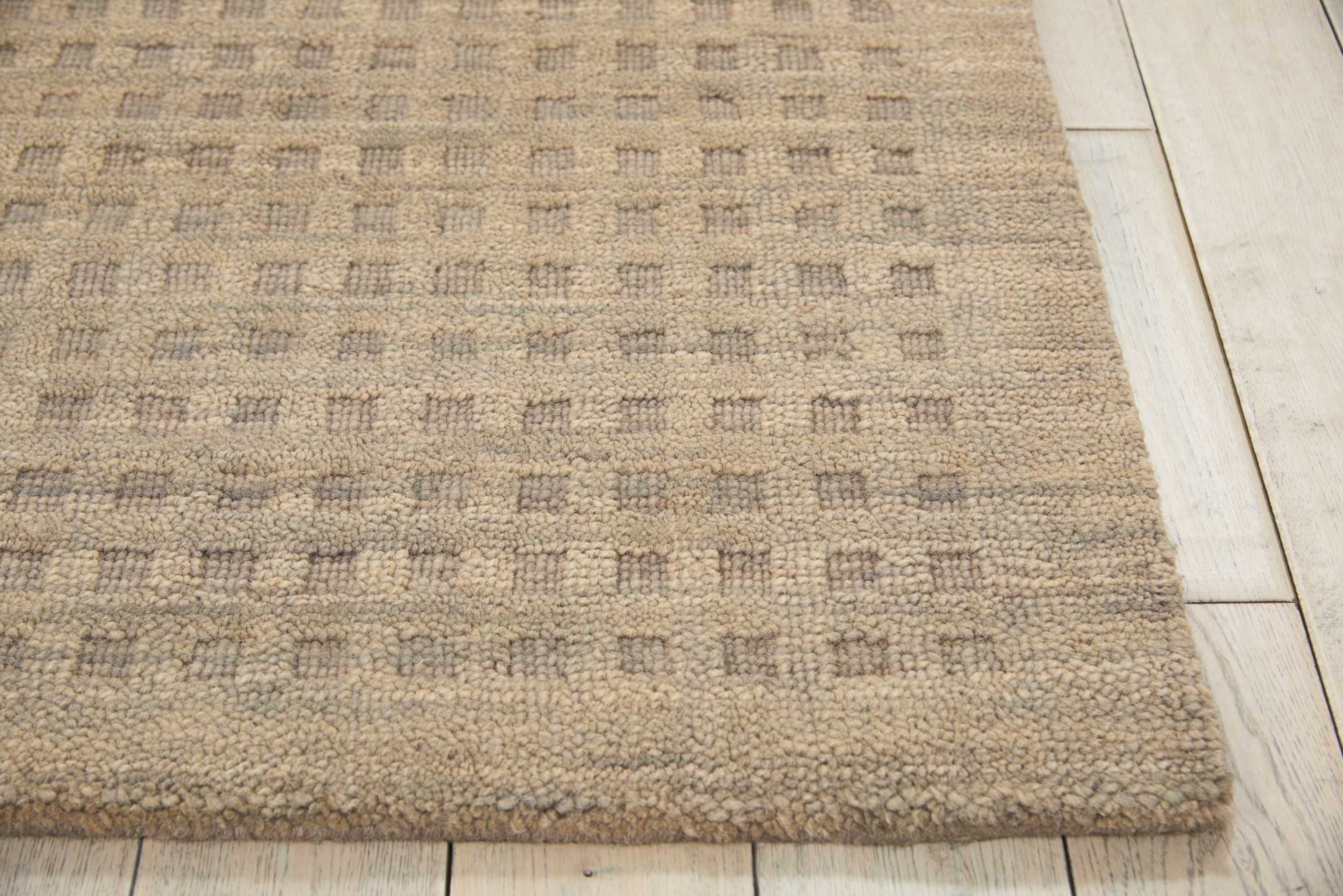 Beige textured rug with a subtle checkered pattern in taupe and gray tones on light wood flooring.