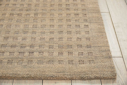 Beige textured rug with a subtle checkered pattern in taupe and gray tones on light wood flooring.
