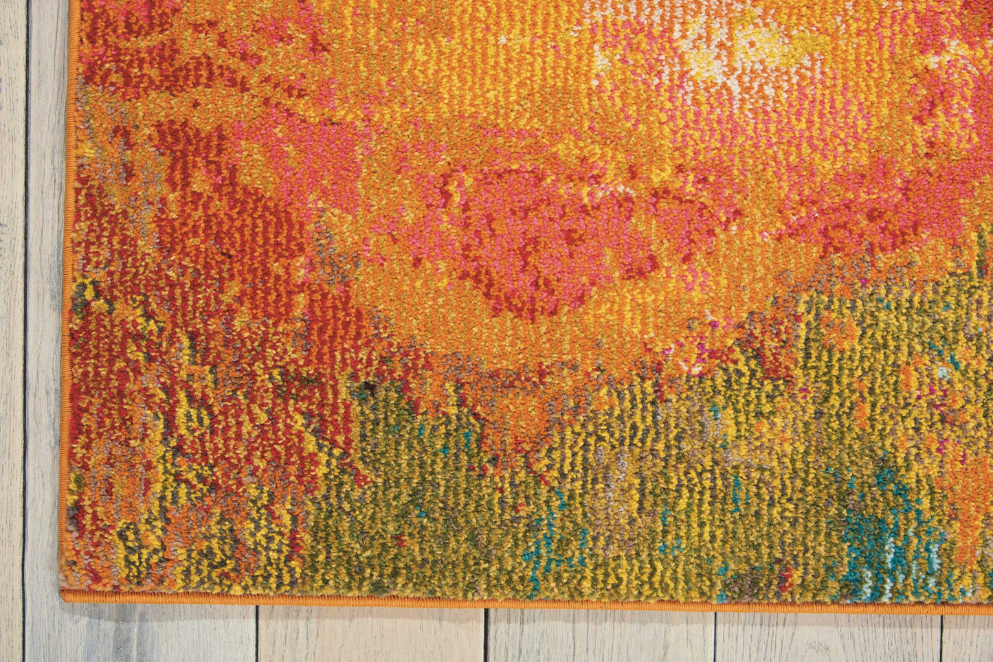 Vibrant abstract, machine-woven area rug in orange, pink, yellow, green and blue hues on a light wood floor.