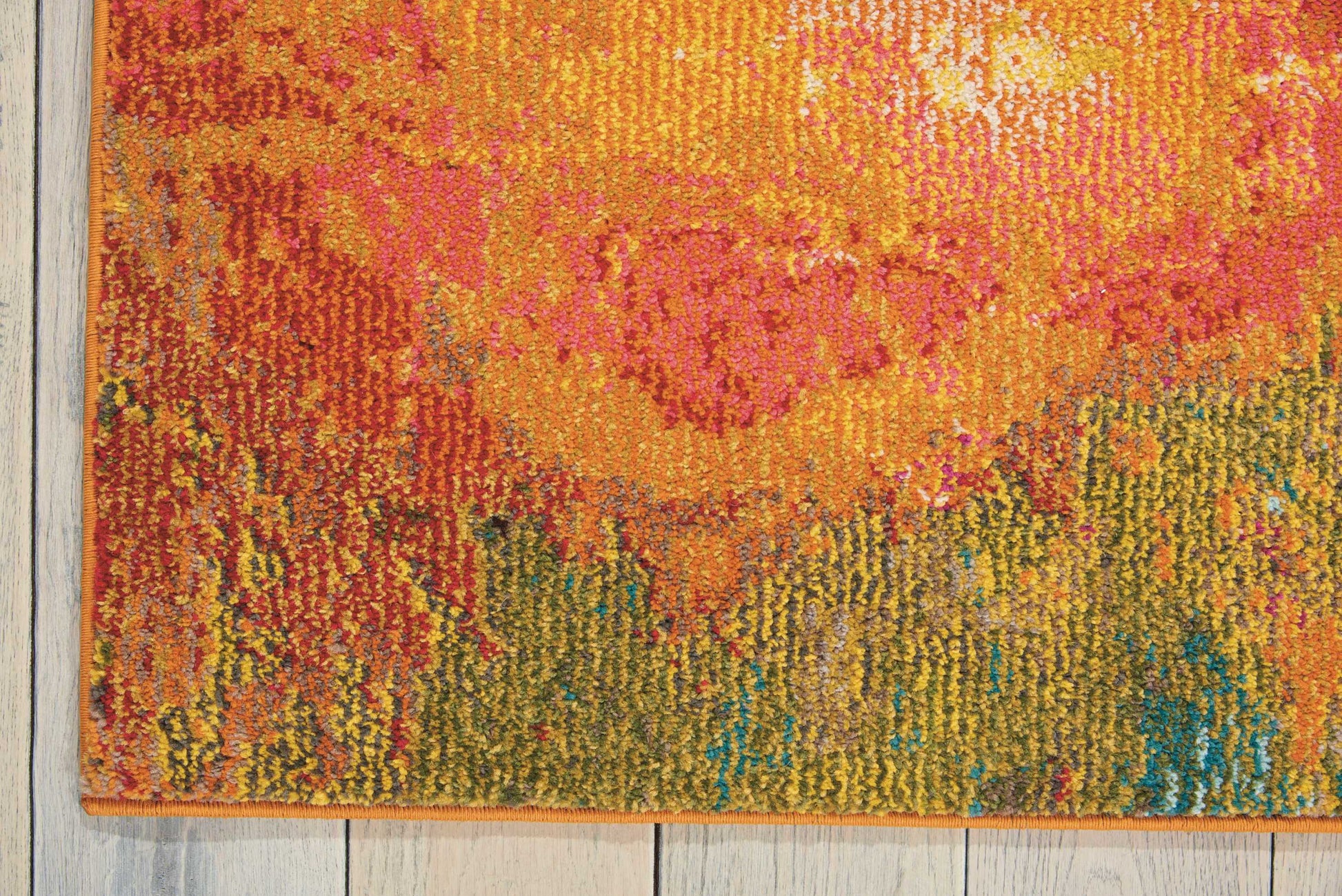 Vibrant abstract, machine-woven area rug in orange, pink, yellow, green and blue hues on a light wood floor.