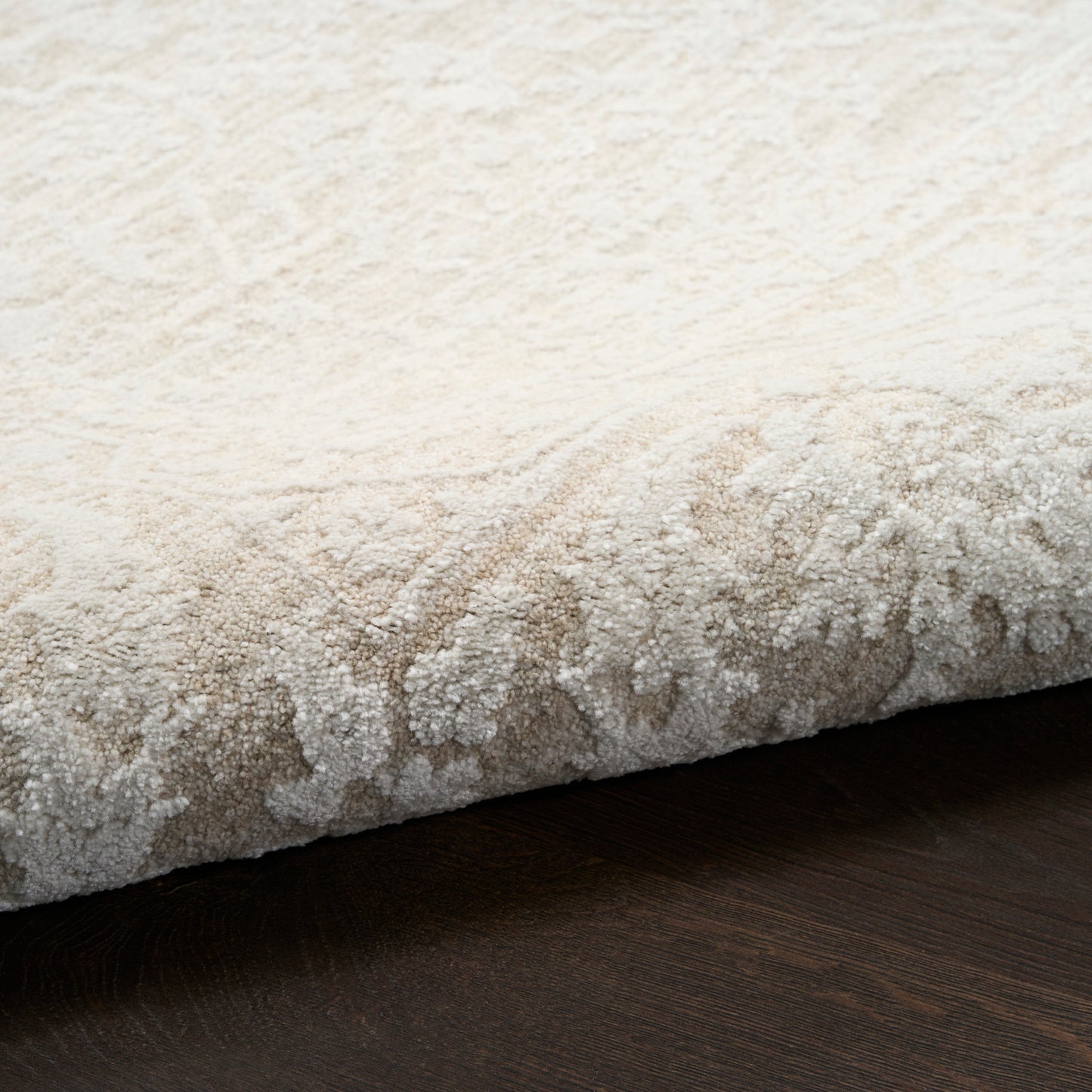 Cream and beige textured high-pile rug with a folded edge on dark wood floor.