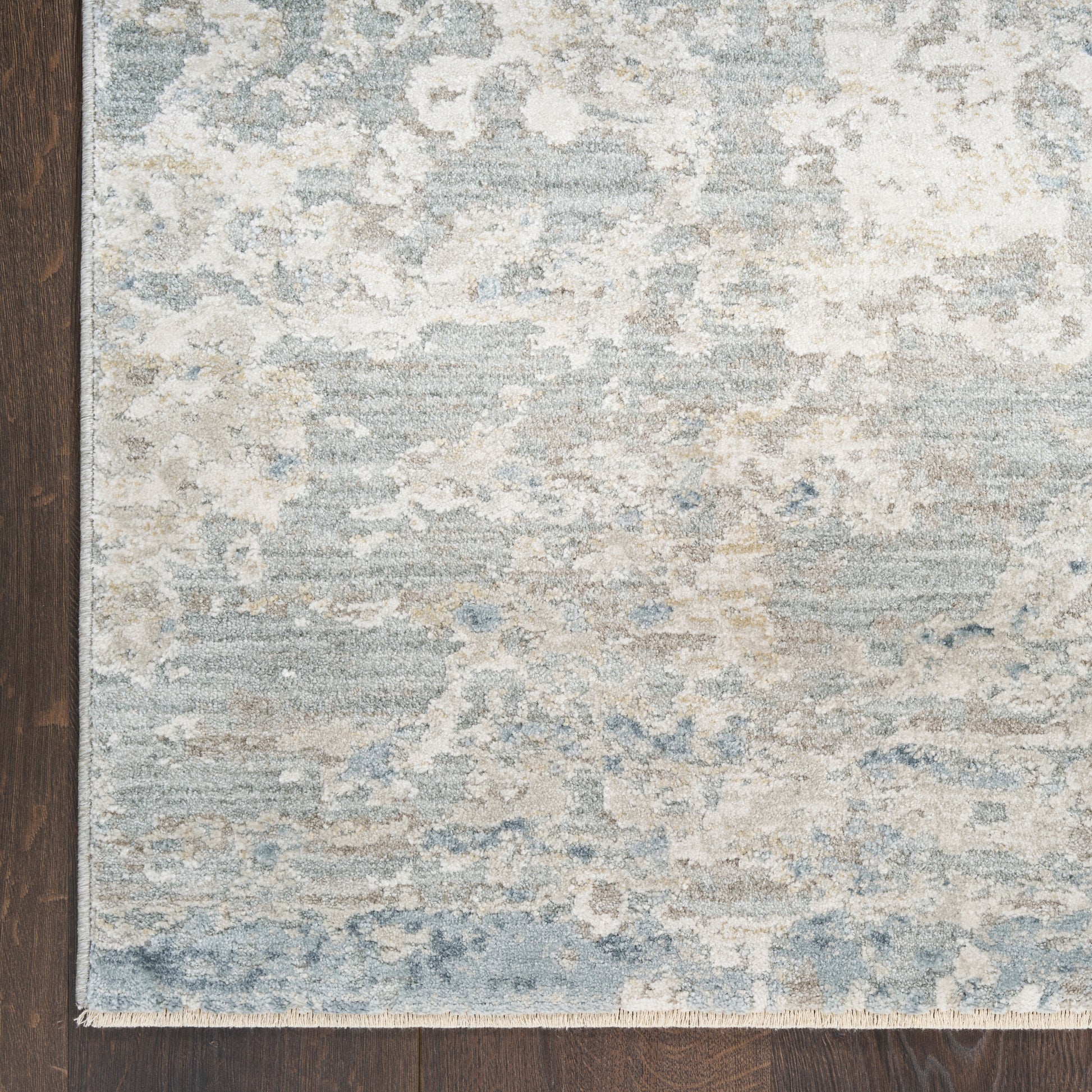 Distressed abstract blue and beige area rug with light fringe on dark wood flooring.