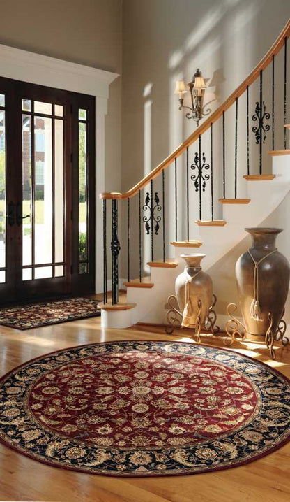 Elegant entryway featuring a curved wood staircase, wrought-iron balusters, dark front doors, a round red Persian-style rug, and vases.