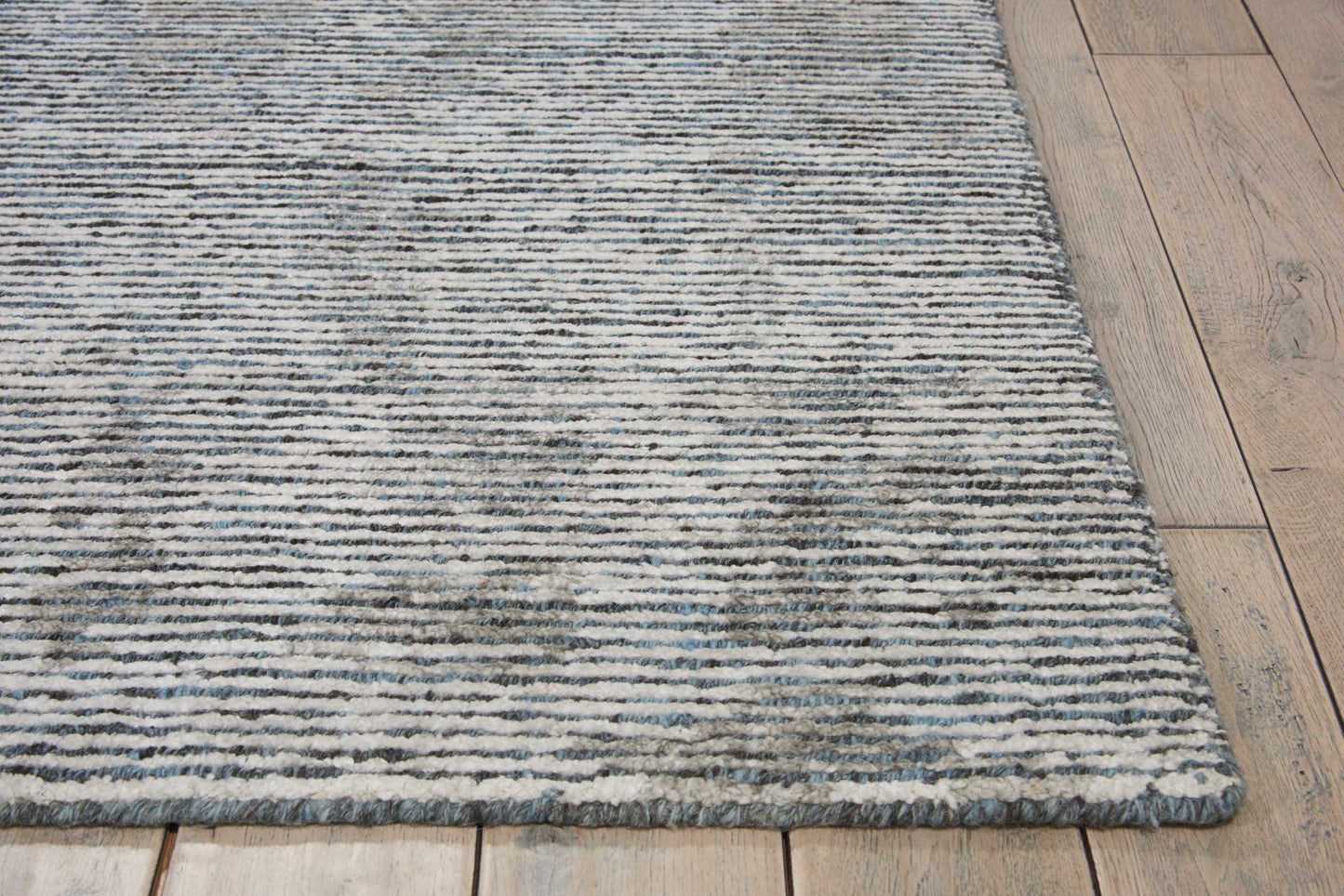 Blue-gray striped flat-weave rug on wooden floor, subtle texture with light and dark bands.
