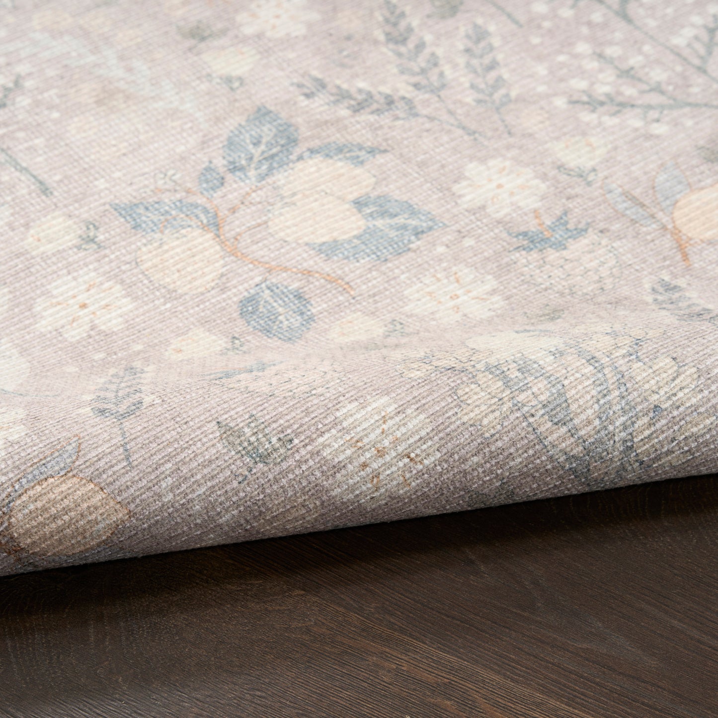 Pastel floral woven rug sample in blues, creams and pinks, rolled edge on dark wood surface.