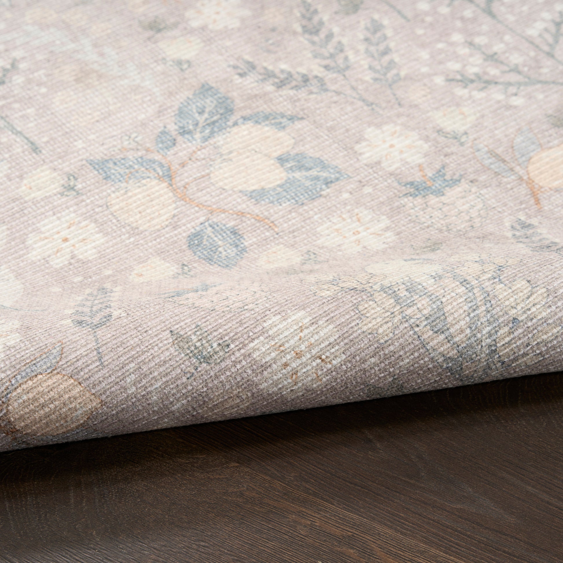 Pastel floral woven rug sample in blues, creams and pinks, rolled edge on dark wood surface.