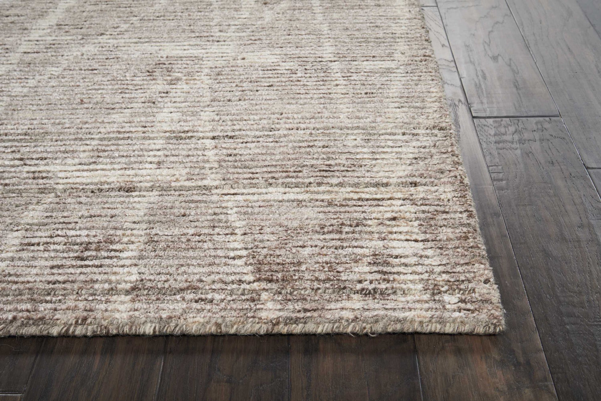 Beige textured low-pile area rug with subtle striped pattern on dark wood floor; neutral modern rustic style.
