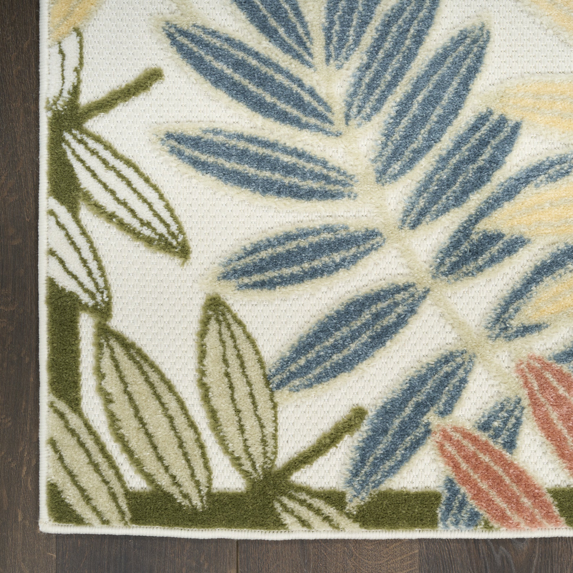Woven rug corner with blue and green palm leaves on cream background; orange-tinted highlights, textured weave.