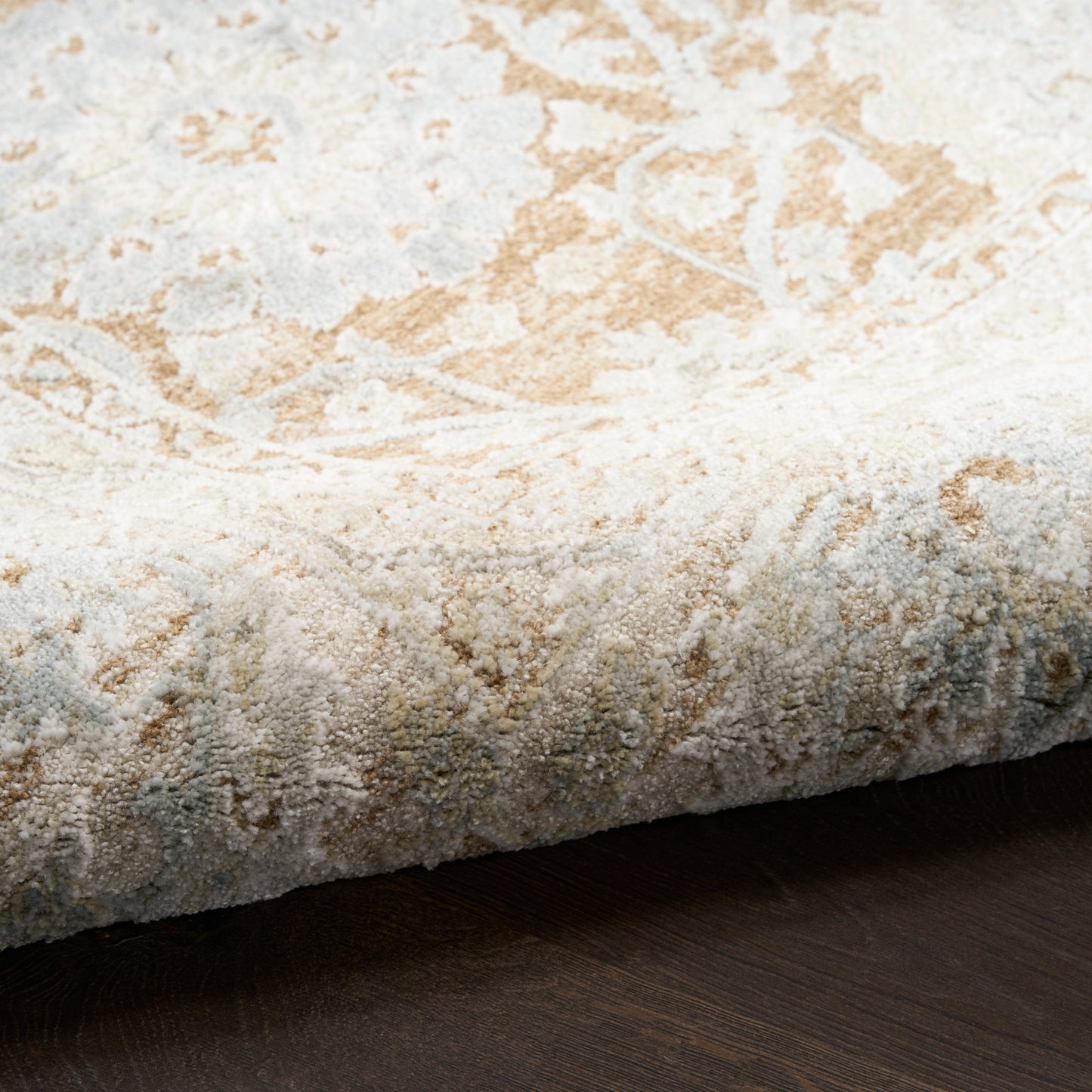 Beige and ivory area rug with a distressed damask pattern and textured pile, edge visible on dark wood floor.