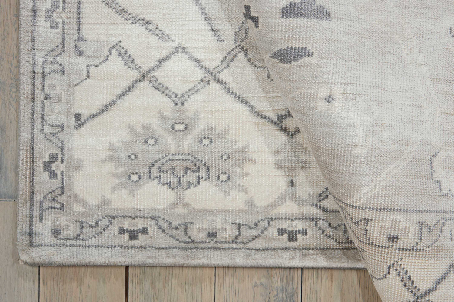 Rectangular light gray-beige woven rug with subtle floral medallion and geometric border on a wood floor.