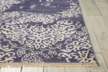 Navy blue area rug with white intricate floral/arabesque pattern and light fringe on a wooden floor.