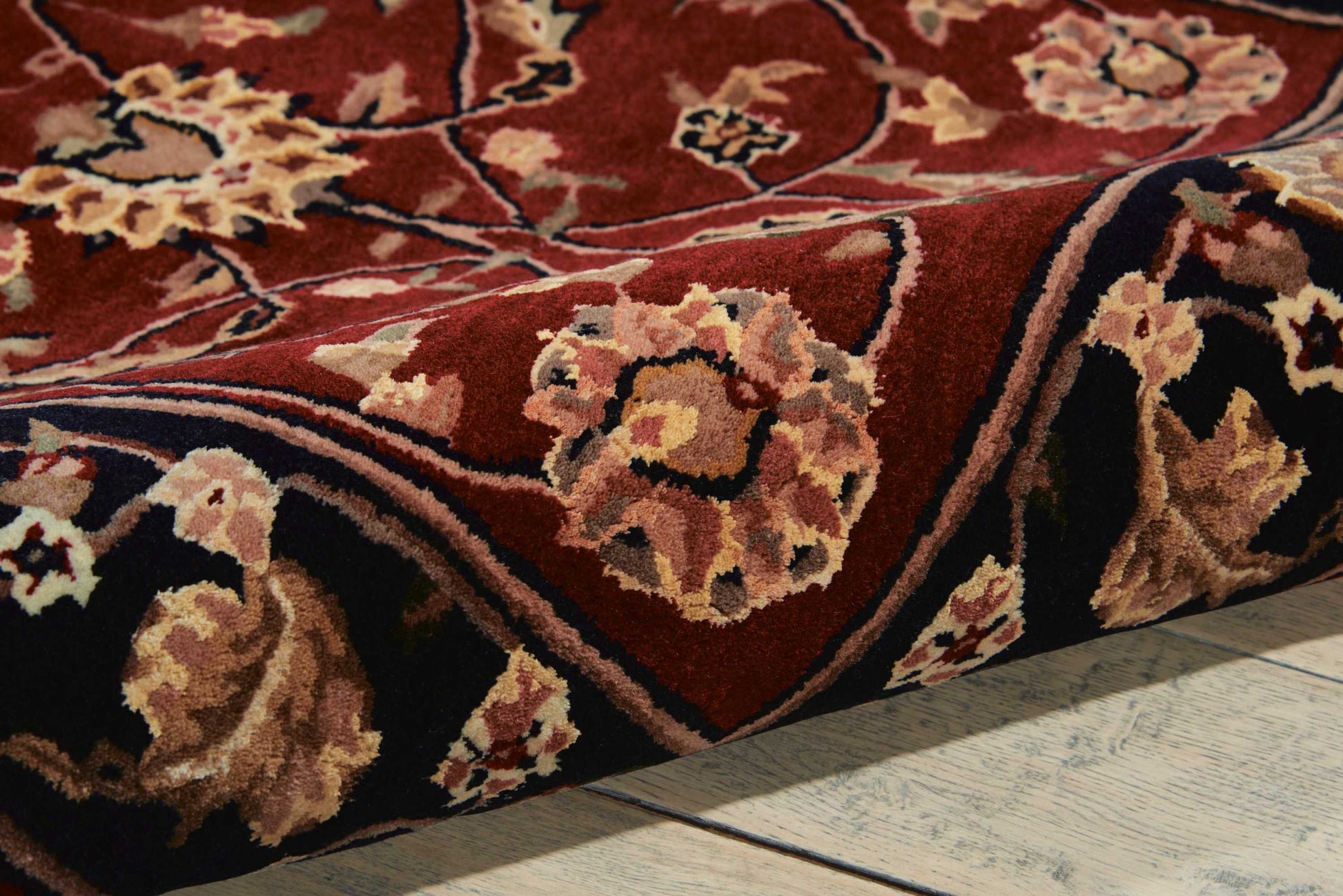 Persian-style floral rug in deep red with cream and tan flowers, wool pile, rolled edge on wood floor.