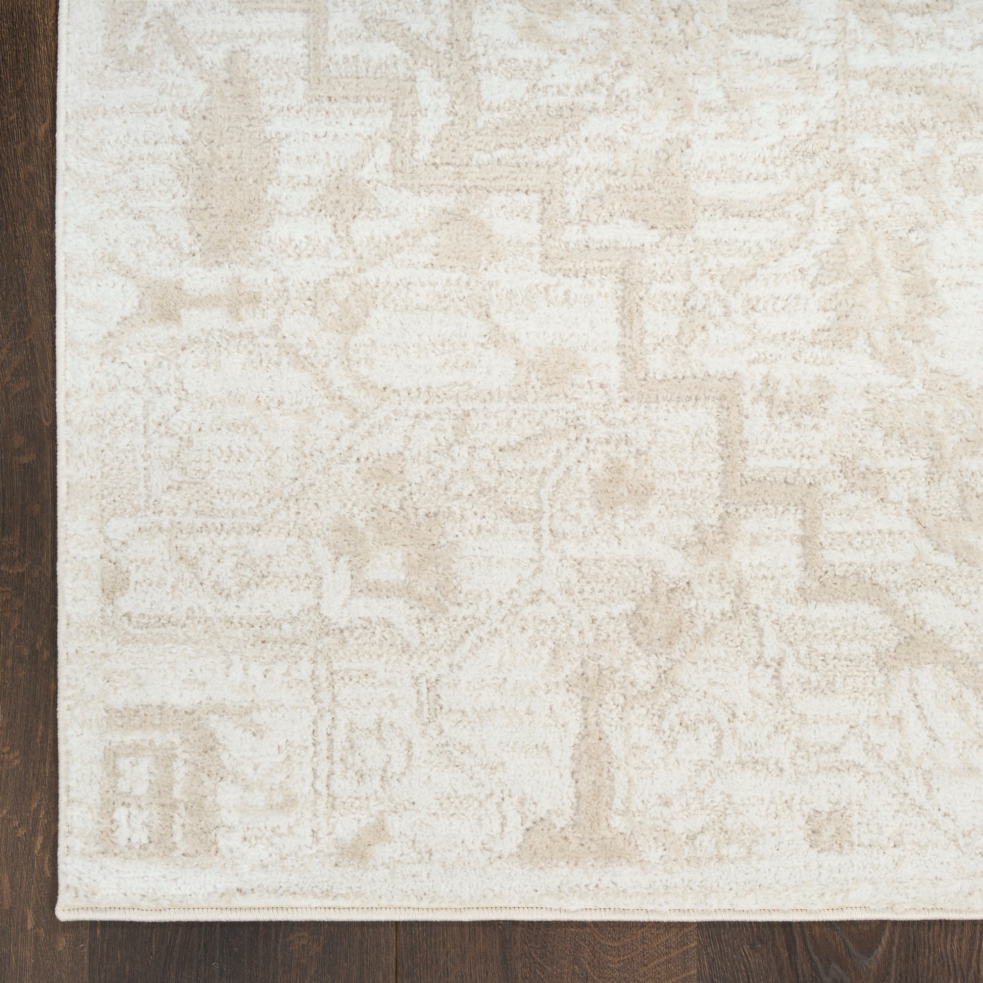 Cream-colored patterned area rug with subtle geometric motifs on dark wood floor.